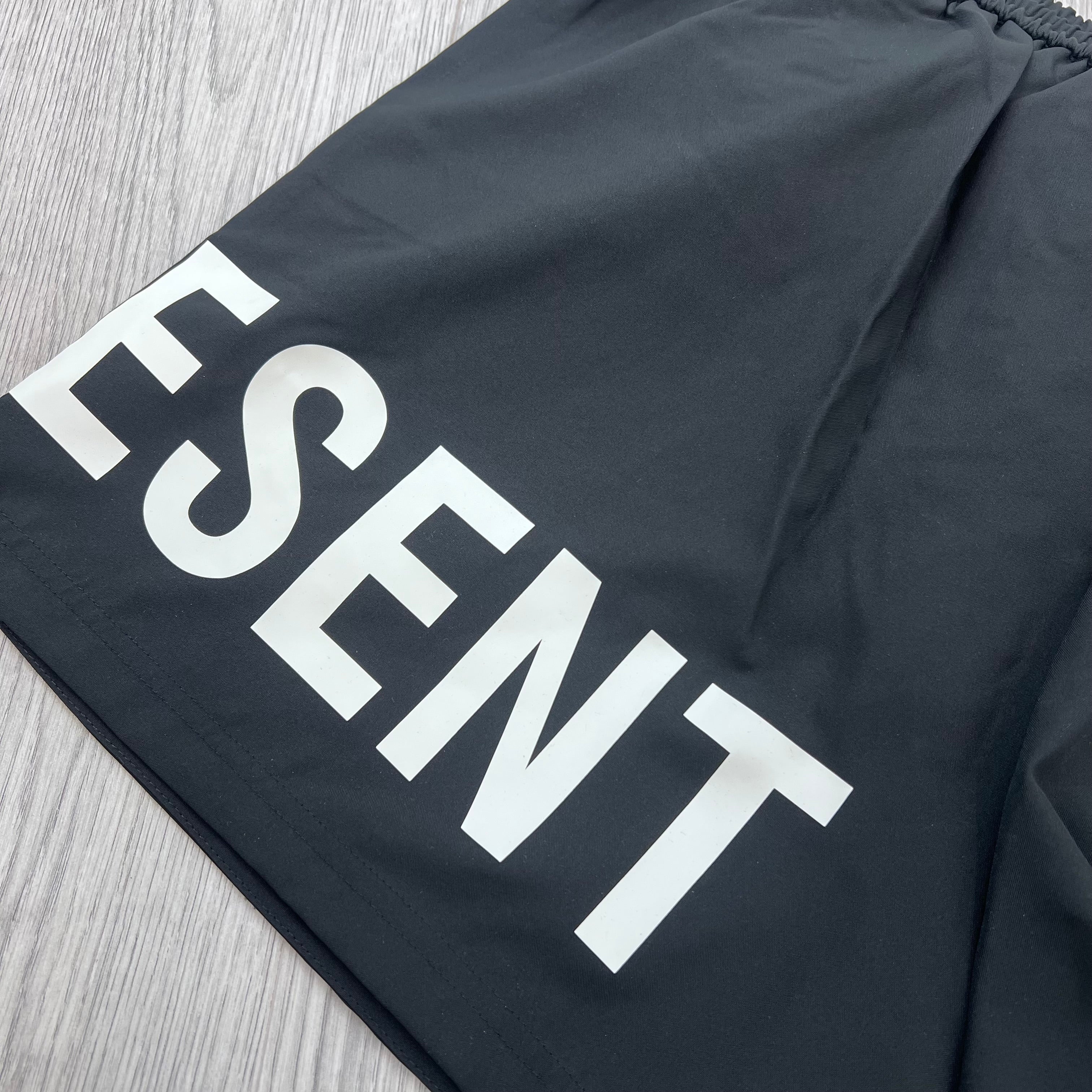 A close up view of the white logo on the back of the Represent Swim Shorts in Black.