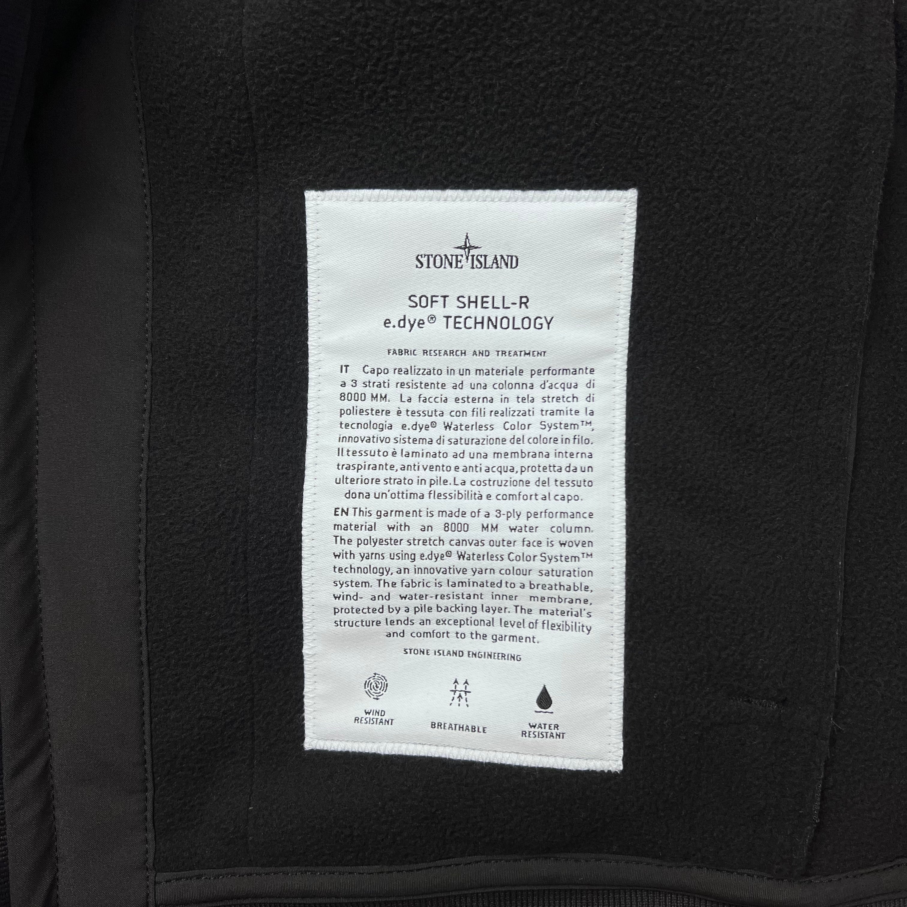 A close up view of the engineering label on the inside of a Stone Island Soft Shell-R_e.dye® Jacket in Black.