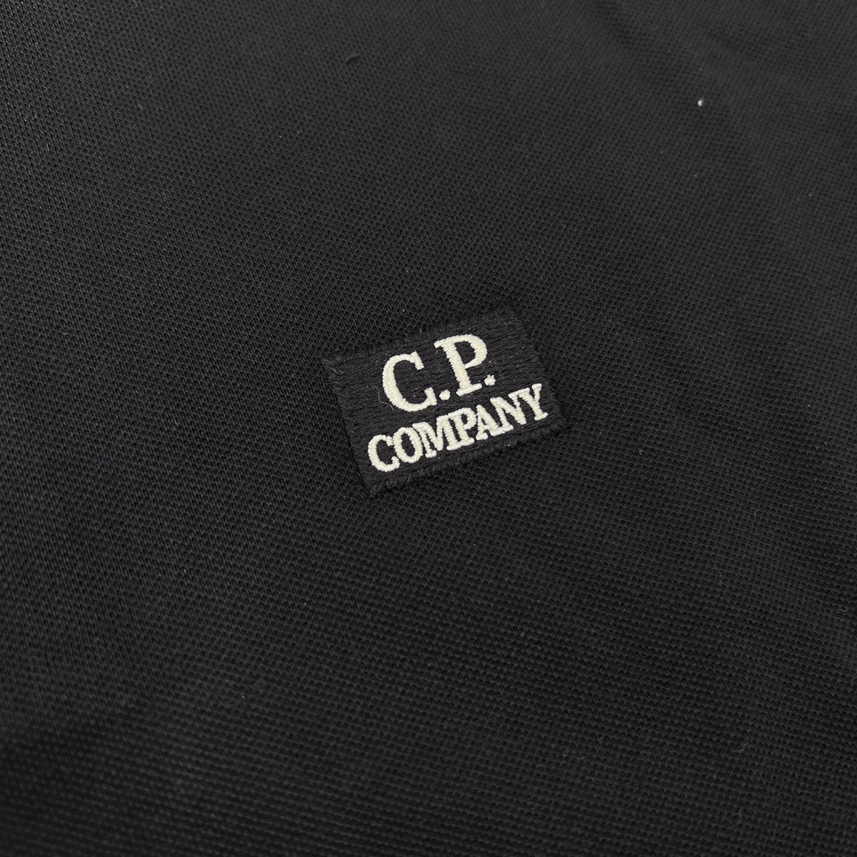Close up view of the embroidered logo detail on a CP Company Stretch Piquet Long Sleeve Polo Shirt in Navy Blue. 