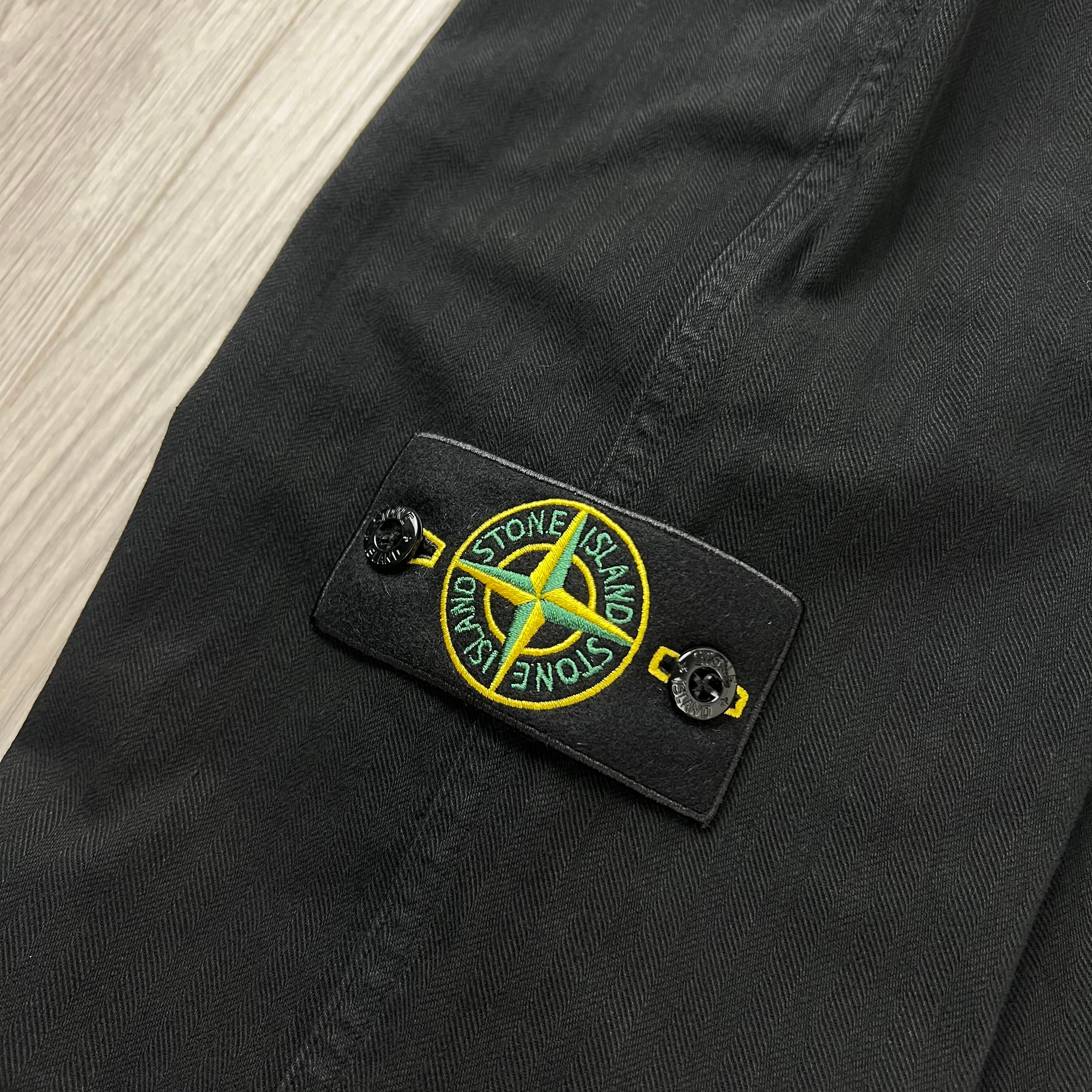 A close up view of the compass badge on the Stone Island Cotton Herringbone Chino Trousers in Black.